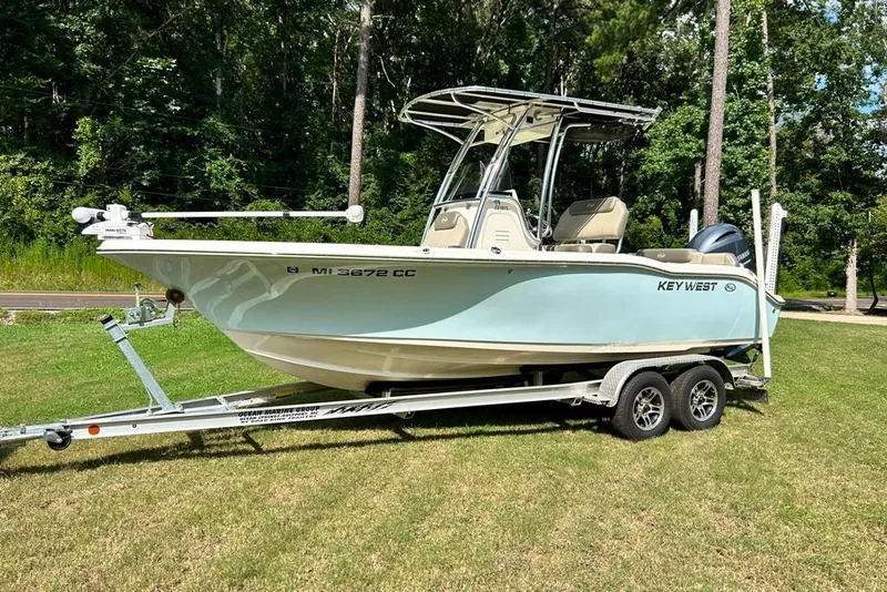 Slide: The Image of 2022 Key West 219 FS boat on trailer, parked on grass with forest background. - 44