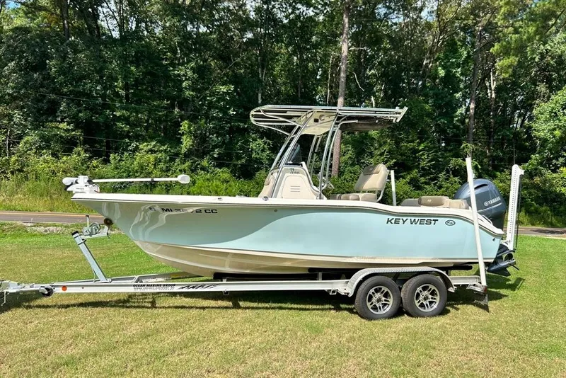 Slide: The Image of 2022 Key West 219 FS boat on trailer, parked on grass with forest background. - 48