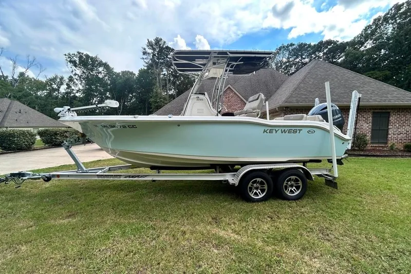 Slide: The Image of 2022 Key West 219 FS boat on trailer, parked on grass, with a house in the background. - 7