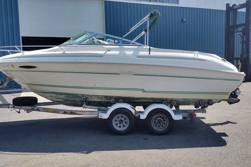 The Image of 1999 Sea Ray 215 Express Cruiser on trailer, parked outside a blue building. - 1