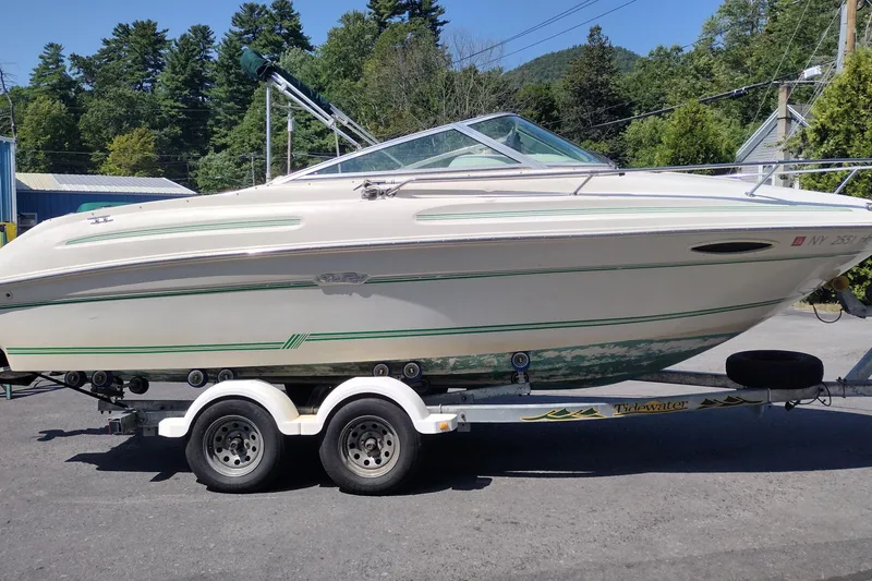 Slide: The Image of 1999 Sea Ray 215 Express Cruiser on trailer, parked outdoors with trees in background. - 3