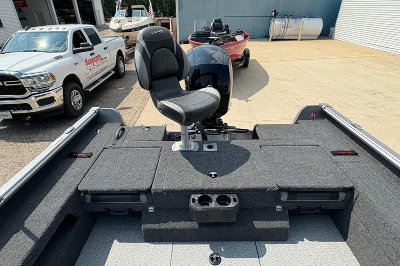 Slide: The Image of 2026 Lund 1875 Impact XS Sport boat interior with seating and storage, parked near a truck. - 34