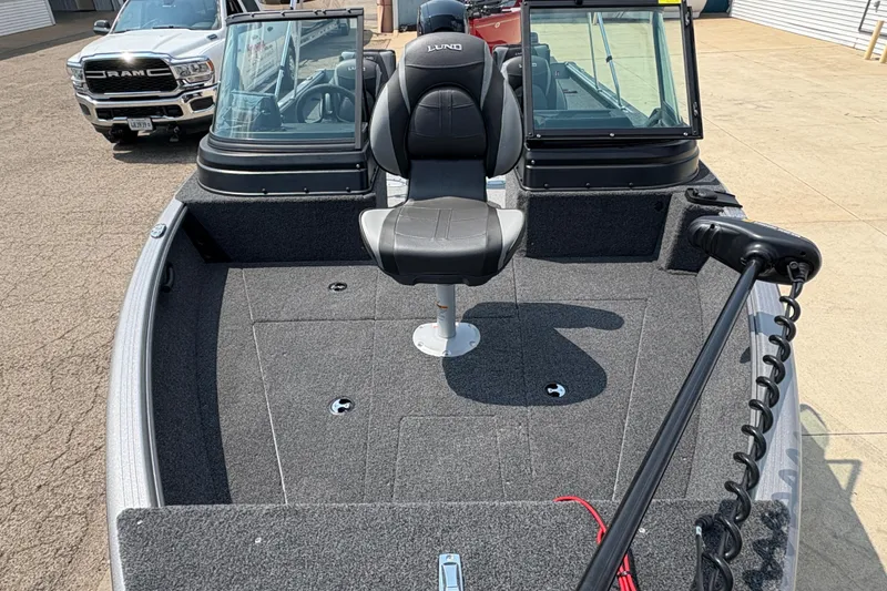 Slide: The Image of 2026 Lund 1875 Impact XS Sport boat interior with seating and windshield, parked near a Ram truck. - 9