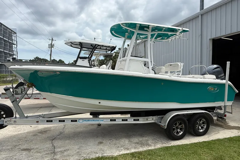 Slide: The Image of 2021 Sea Hunt Ultra 219 boat on trailer, teal hull, parked outside a building. - 14