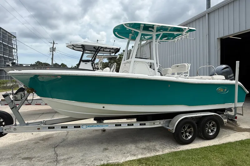 Slide: The Image of 2021 Sea Hunt Ultra 219 boat on trailer, teal hull, parked outside a building. - 17