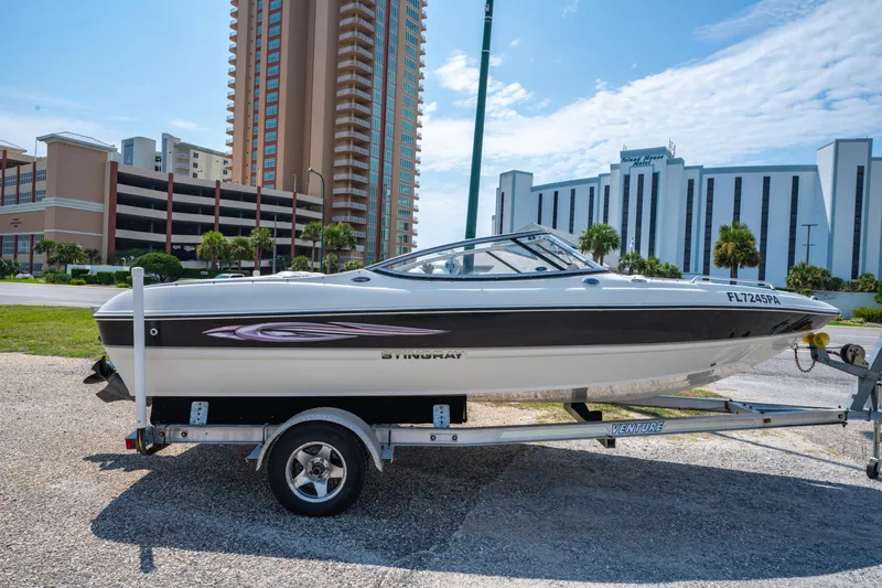 Slide: The Image of 2010 Stingray 195LX boat on trailer, parked near tall buildings under a clear sky. - 3