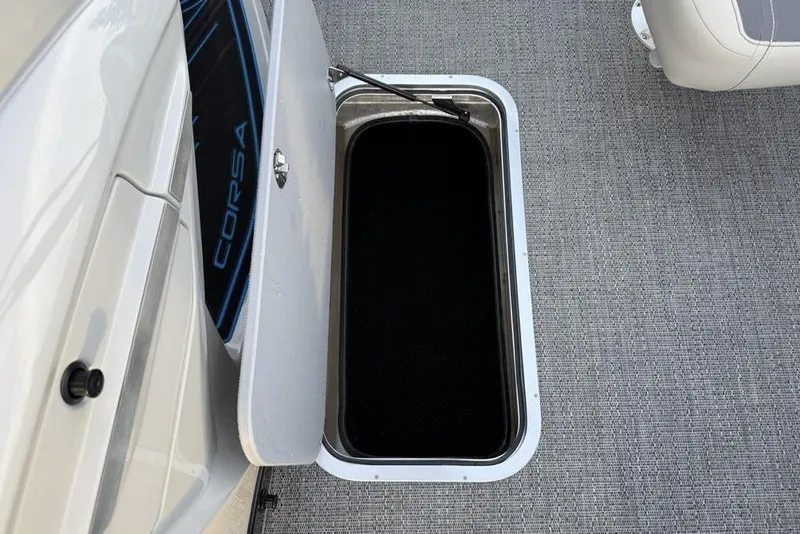 Slide: The Image of 2025 Barletta 23UC boat storage compartment with open hatch on gray carpeted floor. - 16