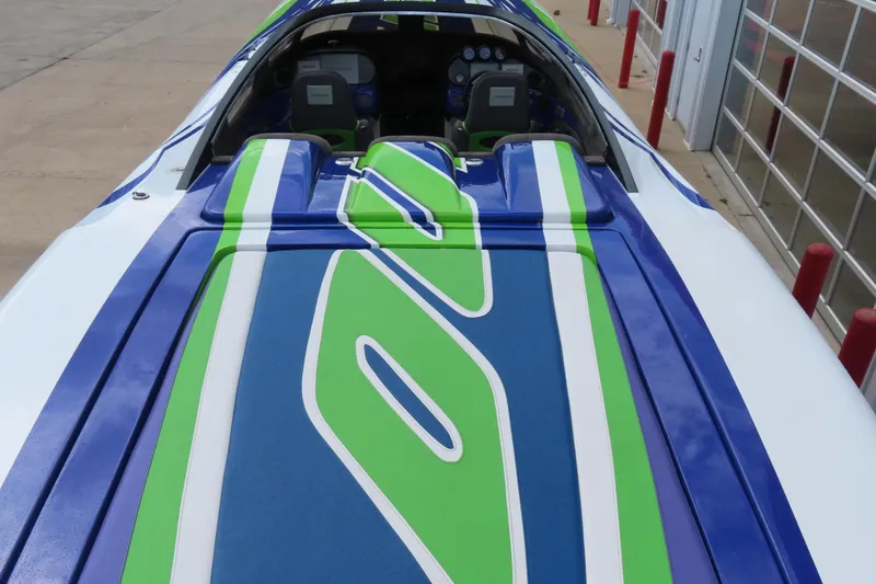 Slide: The Image of 2007 Outerlimits 44 GTX boat with vibrant blue and green design, docked near a garage. - 13