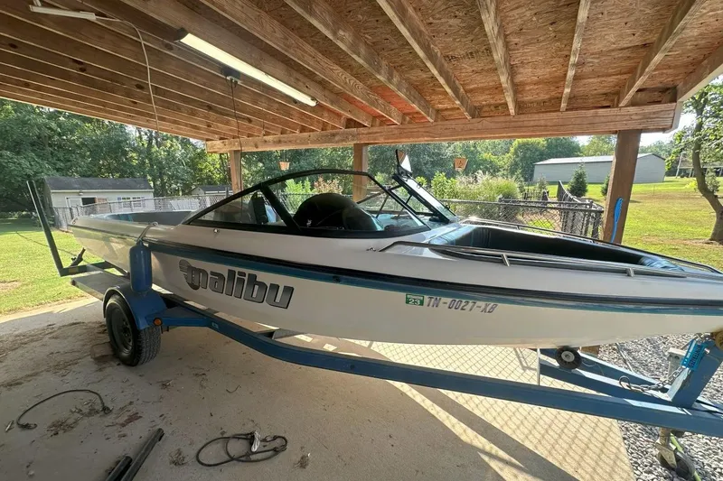 The Image of 1998 Malibu Response boat on trailer under wooden shelter, sunny day. - 0