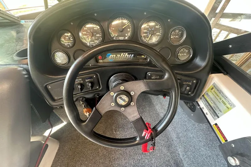 Slide: The Image of 1998 Malibu Response dashboard with steering wheel and gauges in a boat cockpit. - 10