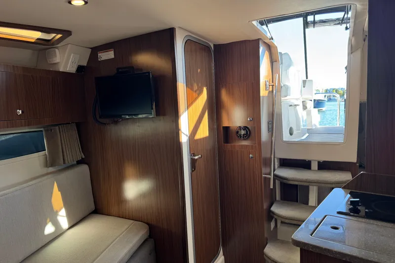 Slide: The Image of 2020 Four Winns Vista 275 cabin interior with wood paneling, TV, and seating area. - 17