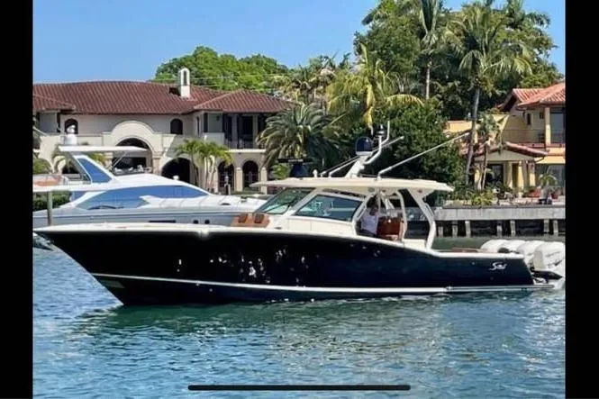 Slide: The Image of 2019 Scout 420 LXF boat cruising near waterfront homes with palm trees. - 5