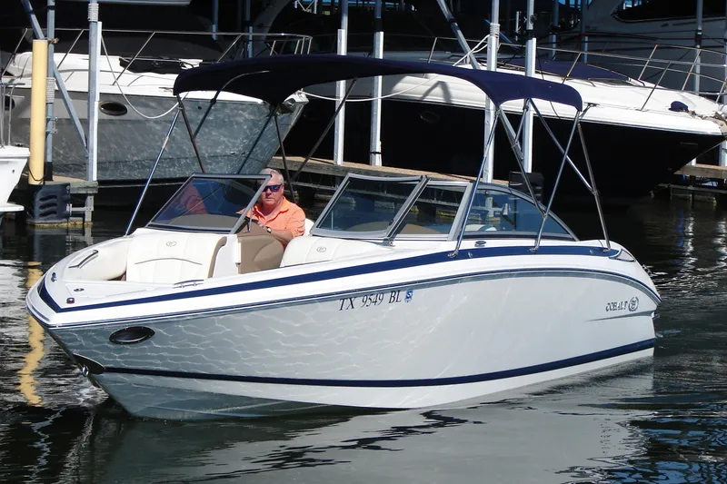 The Image of 2011 Cobalt 232 boat with canopy, docked in marina, man seated at helm. - 0