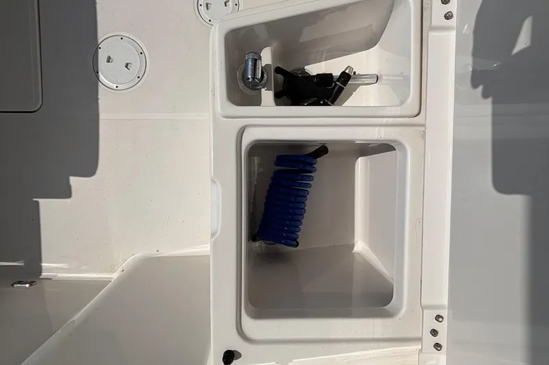 Slide: The Image of 2017 Pursuit DC 235 Dual Console boat storage compartments with coiled blue hose. - 21