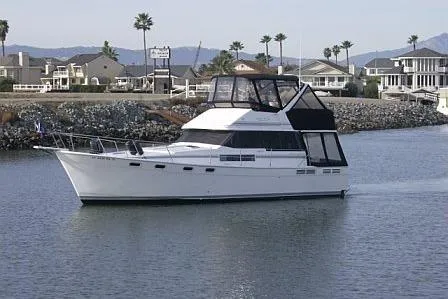 The Image of 1990 Bayliner 3888 yacht cruising in a scenic coastal area with houses and palm trees. - 0