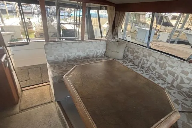 Slide: The Image of 1990 Bayliner 3888 interior with cushioned seating and wooden table, docked at marina. - 17