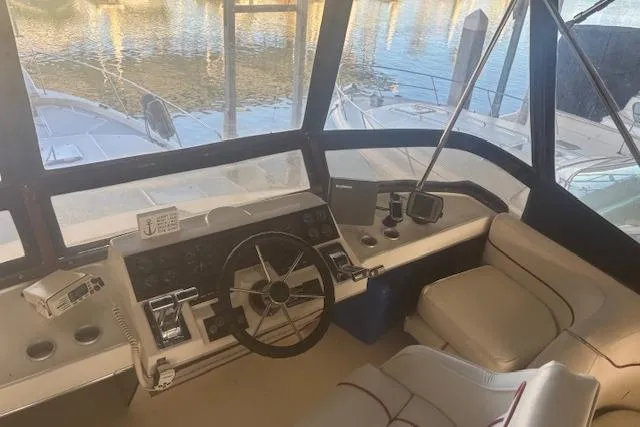 Slide: The Image of 1990 Bayliner 3888 boat cockpit with steering wheel and control panel, docked by the water. - 30