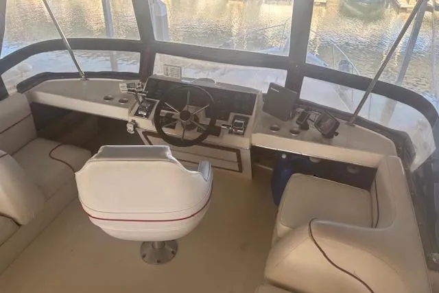 Slide: The Image of 1990 Bayliner 3888 boat cockpit with steering wheel and seating, overlooking water. - 31