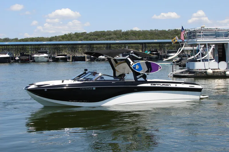 Slide: The Image of 2019 Centurion Ri257 boat on a lake, with wakeboards and marina in background. - 1