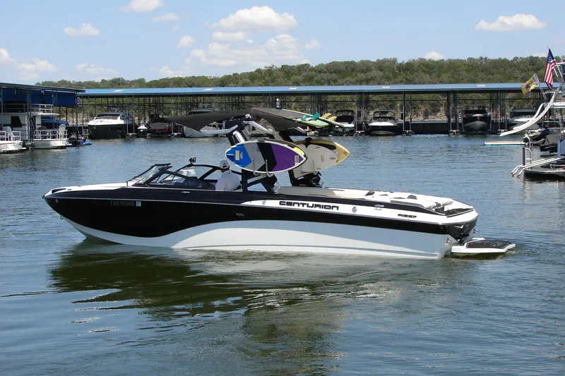 Slide: The Image of 2019 Centurion Ri257 boat on a lake, docked with wakeboards, under a clear sky. - 15