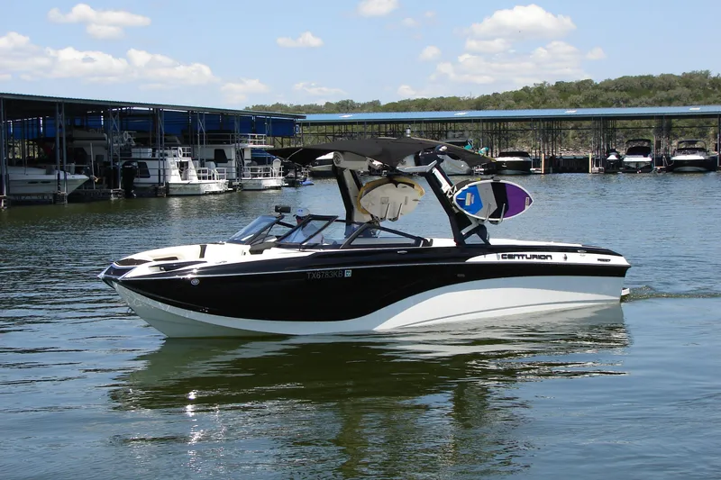 Slide: The Image of 2019 Centurion Ri257 boat docked on a sunny day, featuring sleek black and white design. - 2