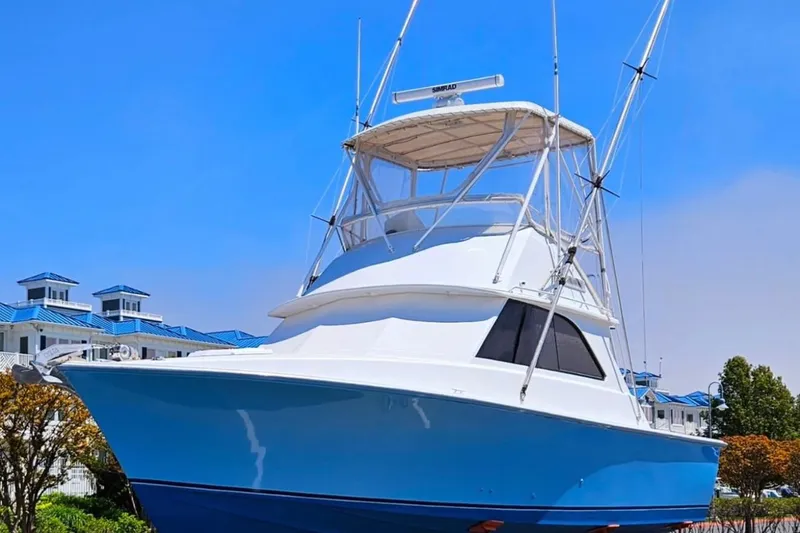 Slide: The Image of 1979 Bertram 35 Flybridge boat with blue hull, docked near buildings under clear sky. - 2