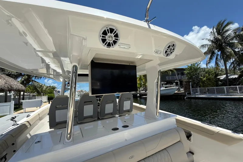 Slide: The Image of 2022 Regal 38 SAV boat interior with seating, TV, and speakers, docked by palm trees. - 30