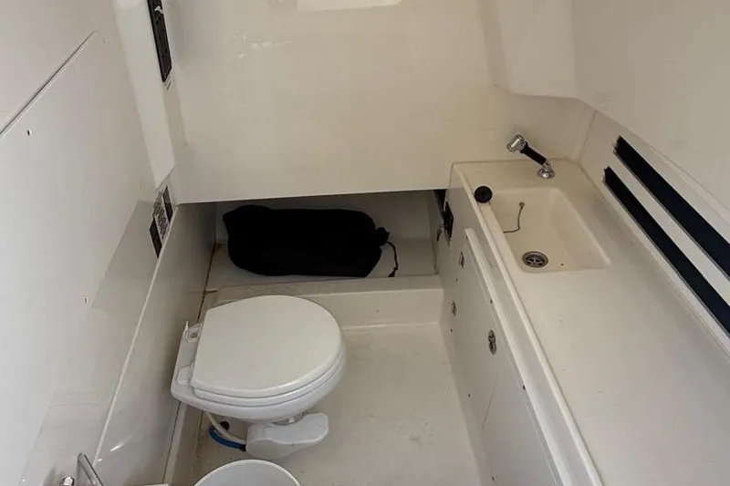 Slide: The Image of 2023 Boston Whaler 330 Outrage cabin with toilet and sink, featuring compact design. - 16