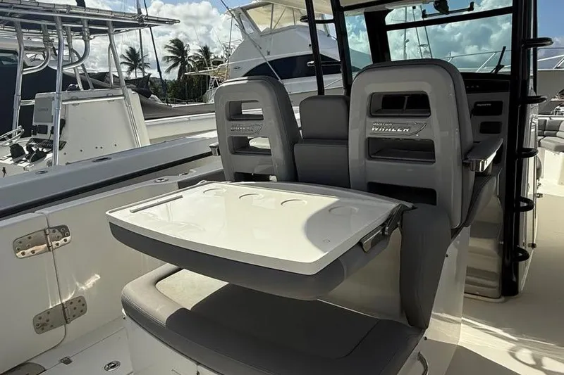 Slide: The Image of 2023 Boston Whaler 330 Outrage boat interior with seating and table, docked near other boats. - 7