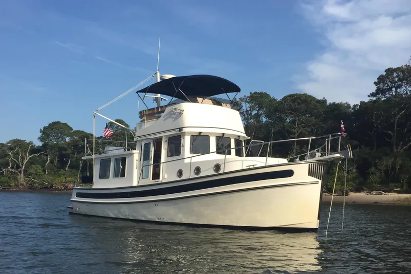 Slide: The Image of 2005 Nordic Tug 37 Flybridge boat on calm water near a wooded shoreline. - 2