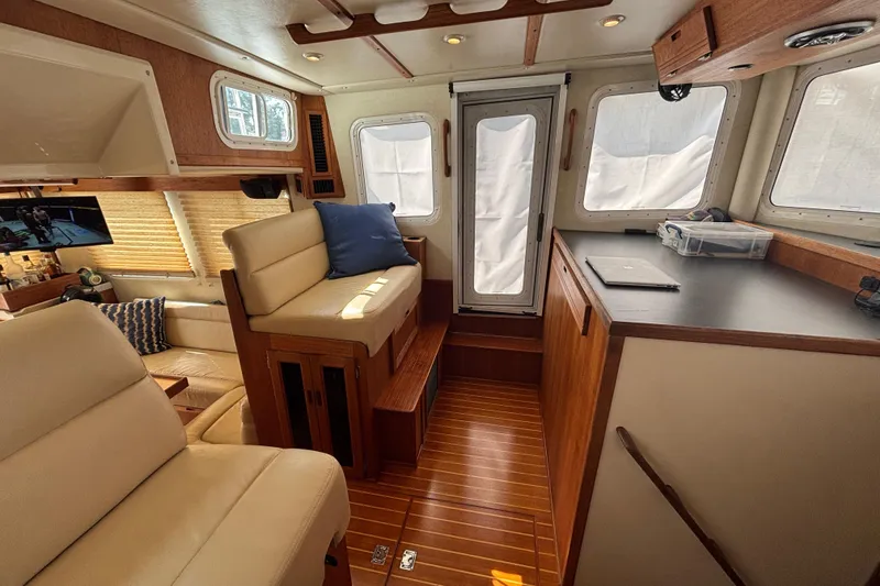 Slide: The Image of Pilothouse of 2005 Nordic Tug 37 Flybridge with cozy seating and wooden accents.  Custom Screen on pilothouse door to port - 37