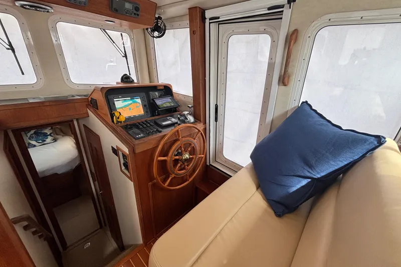Slide: The Image of 2005 Nordic Tug 37 Flybridge interior with helm, navigation equipment, and cozy seating.  Custom Screen on pilothouse door to starboard - 38