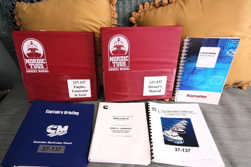 Slide: The Image of Manuals for 2005 Nordic Tug 37 Flybridge, including owner's and engine guides, displayed on a sofa. - 64