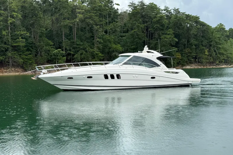 The Image of 2007 Sea Ray 48 Sundancer yacht on tranquil water, surrounded by lush forest. - 0