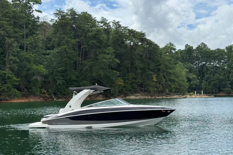 Slide: The Image of 2018 Regal 2500 Bowrider boat cruising on a serene lake with forested shoreline. - 6