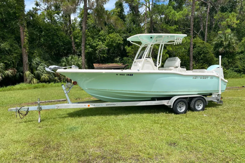 Slide: The Image of 2023 Key West 239 FS boat on trailer, parked on grass with forest background. - 2