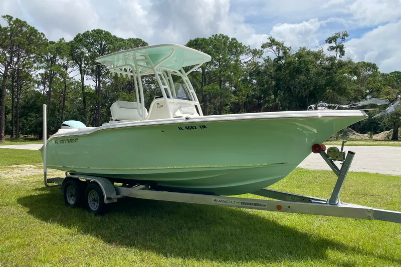 Slide: The Image of 2023 Key West 239 FS boat on trailer, parked on grass with trees in background. - 7