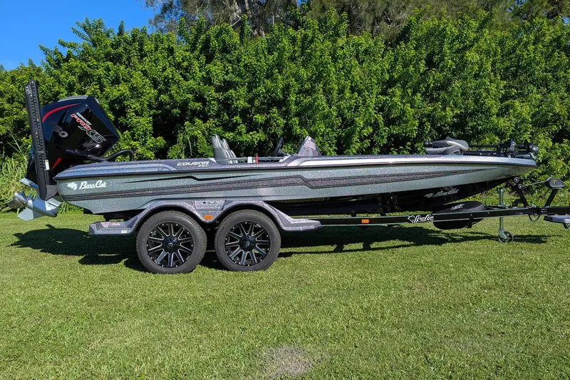 Slide: The Image of 2026 Bass Cat Cougar FTD SP boat on trailer, parked on grass with lush greenery background. - 0