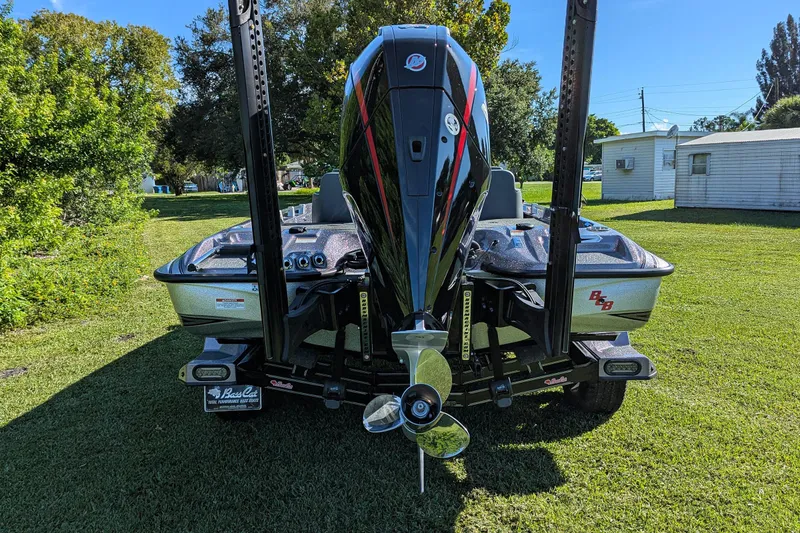 Slide: The Image of 2026 Bass Cat Cougar FTD SP boat, rear view, on grass with trees and buildings. - 7