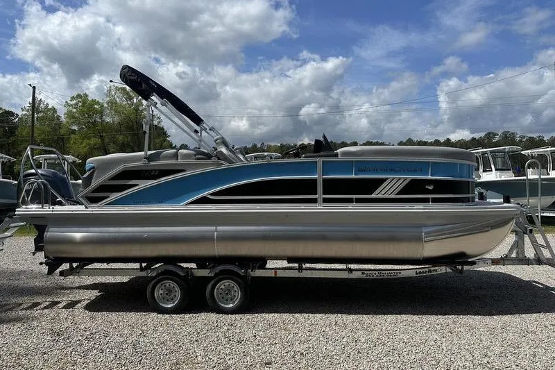 Slide: The Image of 2025 Bennington 22M pontoon boat on trailer, parked outdoors under cloudy sky. - 2