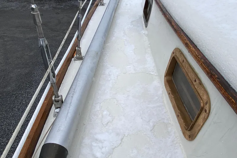 Slide: The Image of 1972 Bristol 40 sailboat deck with snow, showcasing wooden trim and metal fittings. - 27