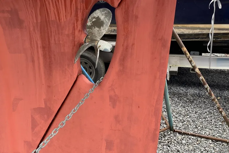 Slide: The Image of 1972 Bristol 40 sailboat propeller and rudder on gravel, with visible chain and support. - 6