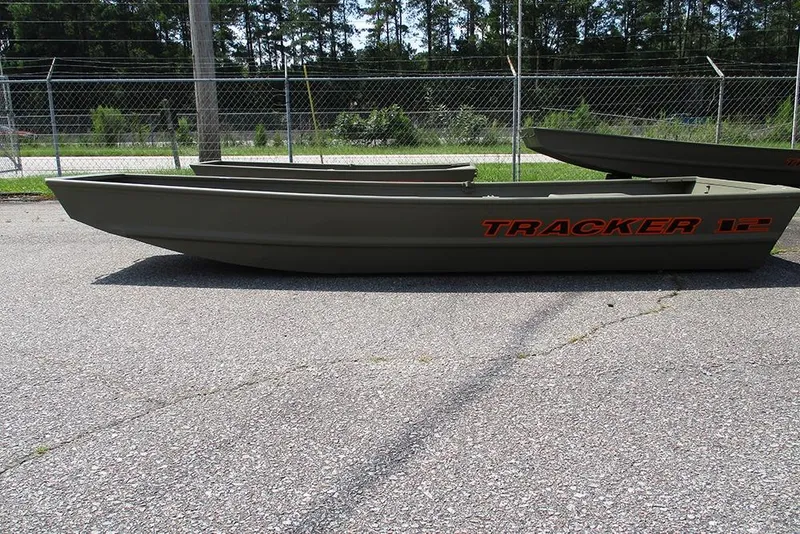 Slide: The Image of 2026 Tracker Grizzly 12 Jon boat on pavement, side view, with trees and fence background. - 6