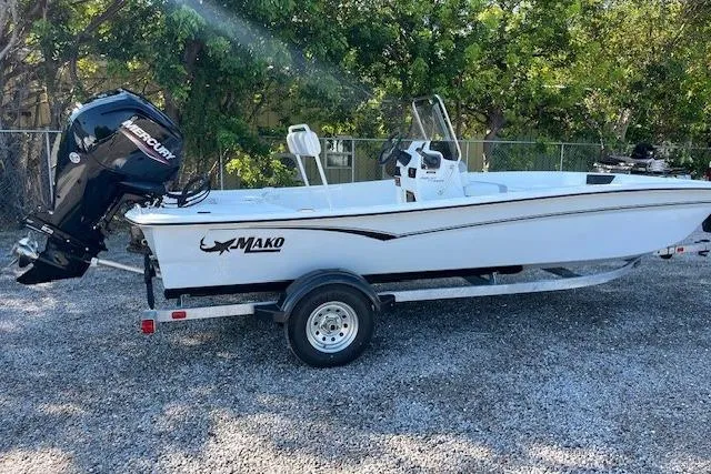 Slide: The Image of 2026 Mako Pro Skiff 17 CC boat with Mercury engine on trailer, parked near a thatched building. - 2