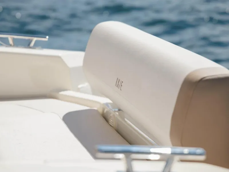 Slide: The Image of 2025 Axopar AX/E 22 T-Top boat interior with beige seating, ocean in background. - 3