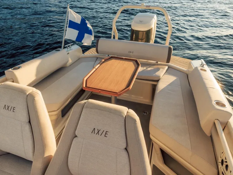 Slide: The Image of 2025 Axopar AX/E 22 T-Top boat interior with seating and table, Finnish flag visible. - 2