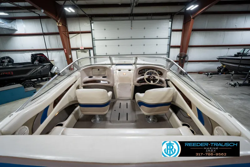 Slide: The Image of Interior of a 2000 Bryant 196 Limited boat in a showroom, featuring beige and blue seating. - 17