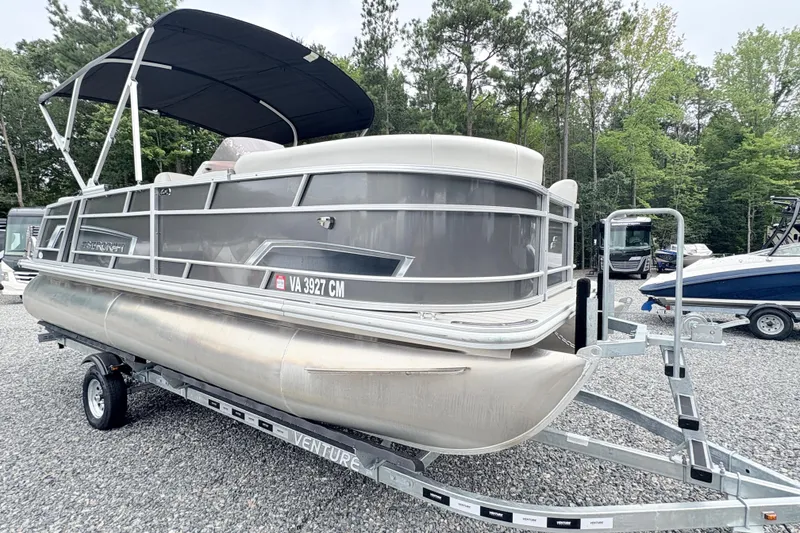 Slide: The Image of 2024 Starcraft 20 EX QDH pontoon boat on trailer, parked on gravel lot. - 2