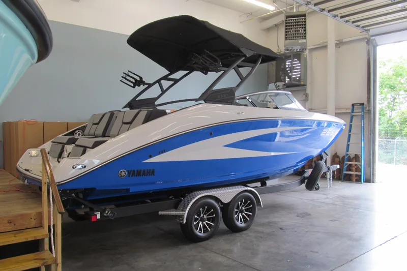 Slide: The Image of 2025 Yamaha Boats 255XD in showroom, blue and white design, on trailer. - 2