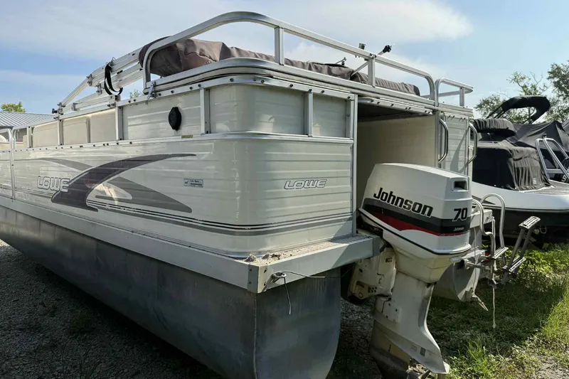 The Image of 1997 Lowe 240 Family pontoon boat with Johnson 70 outboard motor, parked on gravel. - 1